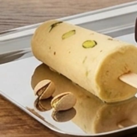 A pistachio kulfi on a stick, with pistachios beside it